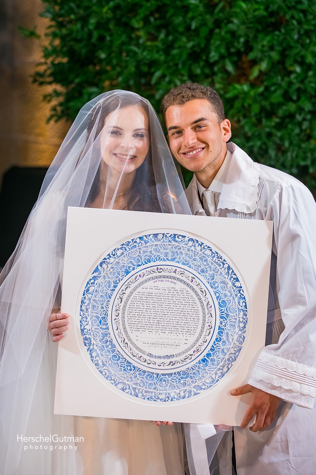 A smiling couple holding their newly received custom Ketubah, their faces radiating with joy.